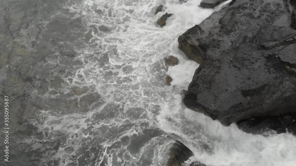 Breathtaking top view of big waves crashing into the black volcanic rocks cliff with splashing and white foam in the restless ocean in Bali, Indonesia Breathtaking top view of big waves crashing into the black volcanic rocks cliff with splashing and white foam in the restless ocean in Bali, Indonesia