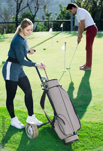 Woman golfer deciding on right club while her male partner hitting ball