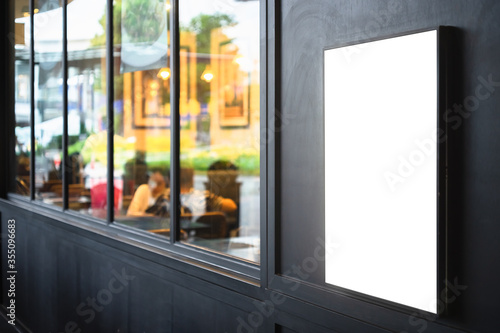 Принти на полотні Mockup blank white screen outdoor advertise lightbox mounted on the black wall of a building with blurred restaurant background