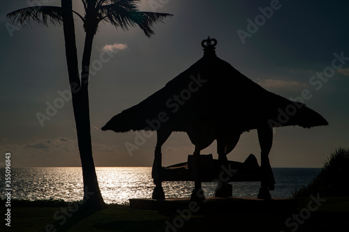 Sun shines through coconut trees and pavilion on the beach