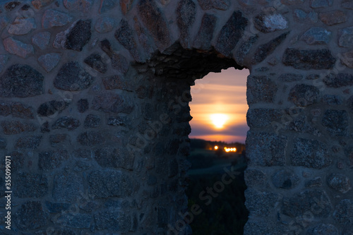 Looking through door in old stone brick wall of castle ruin with setting full moon in distant background