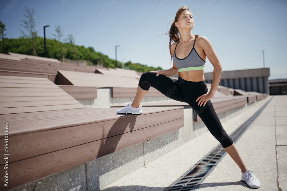 Pilates trainer does exercises on street in park for stretching the inner muscles of the hips and quadriceps leaning on a bench.