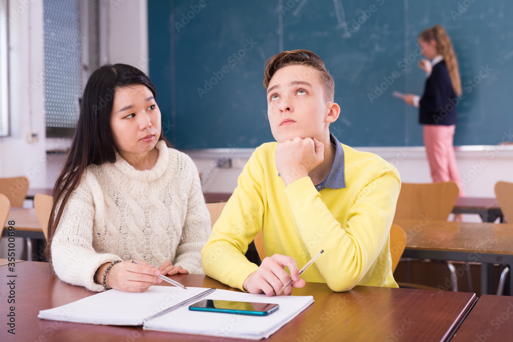 Fototapeta premium Chinese girl student explaining learning material to bored classmate