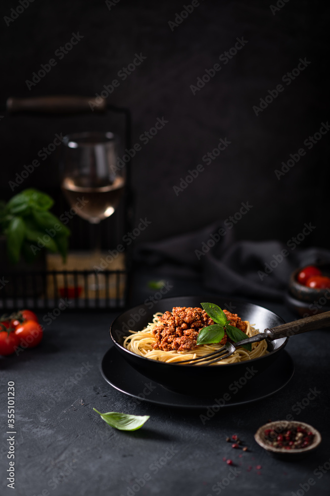 Italian pasta. Spaghetti bolognese in a black bowl on a dark background. In the background a glass of wine. Italian pasta. Spaghetti bolognese in a black bowl on a dark background. In the background a glass of wine.