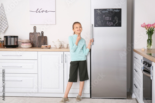Little girl near refrigerator in kitchen