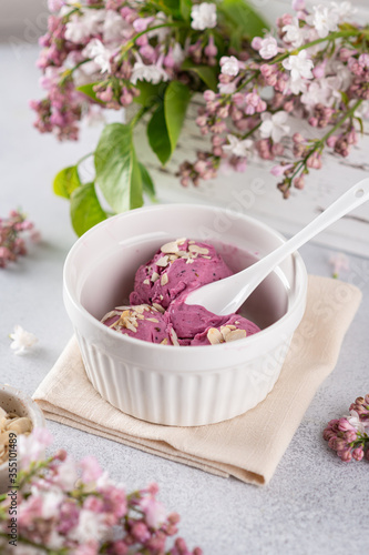lilac ice cream in a white bowl. In the background is a pink lilac. 