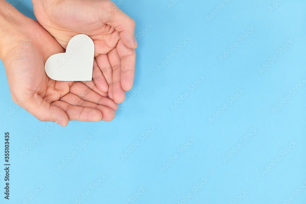 Cupped hands holding a white heart in blue background. Charity, pure ...