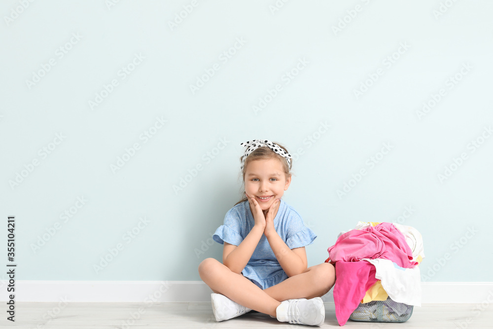 Little girl with dirty laundry sitting near light wall Little girl with dirty laundry sitting near light wall