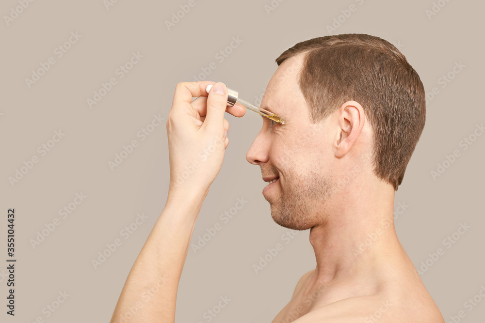 Man skin care routine. Oil pipette near male face. Haircare facial treatment. Applying healthy cosmetics. Anti wrinkles procedure. Grey background Man skin care routine. Oil pipette near male face. Haircare facial treatment. Applying healthy cosmetics. Anti wrinkles procedure. Grey background