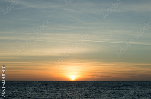 オレンジ色の太陽が水平線に半分隠れる夕焼け空 © Ta-c