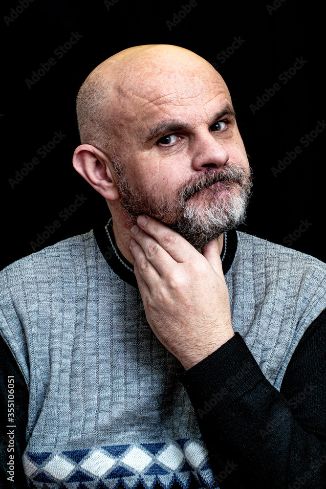 Obraz premium black man with gray beard on the black background scratches his beard with his hand