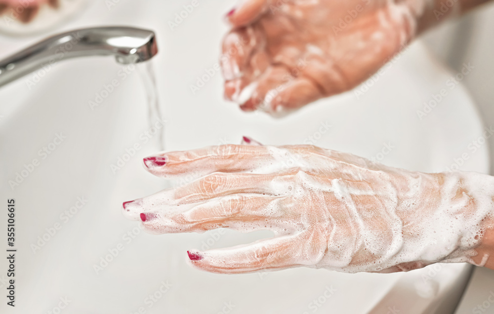 Fototapeta premium Young woman washing her hands under water tap faucet with soap. Detail on suds covered skin. Personal hygiene concept