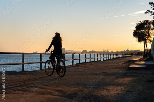Silhouette of young curly girl riding a bicycle at the sunset on the promenade road of Maresme, Catalonia, Spain.