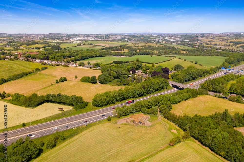 Aerial drone photo of the UK village of Cleckheaton in Bradford West Yorkshire in the UK showing farmers fields along side the M63 Motorway in a bright sunny summers day