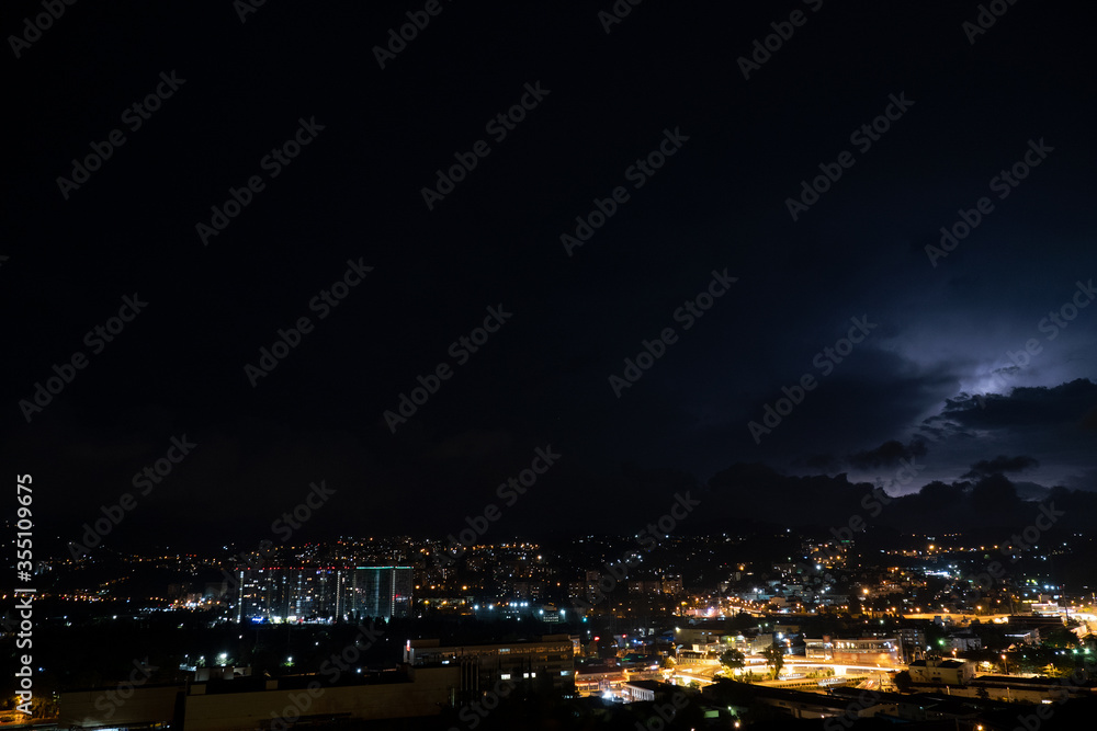 Night landscape. Thunderstorm in the mountains above the night city. Light haze over the city lights.
