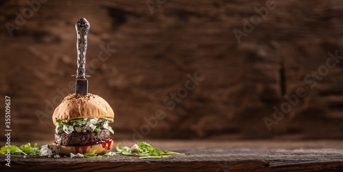 Beef burger with arugula, blue cheese and cranberry saucen with a vintage knife stabbed from the top photo