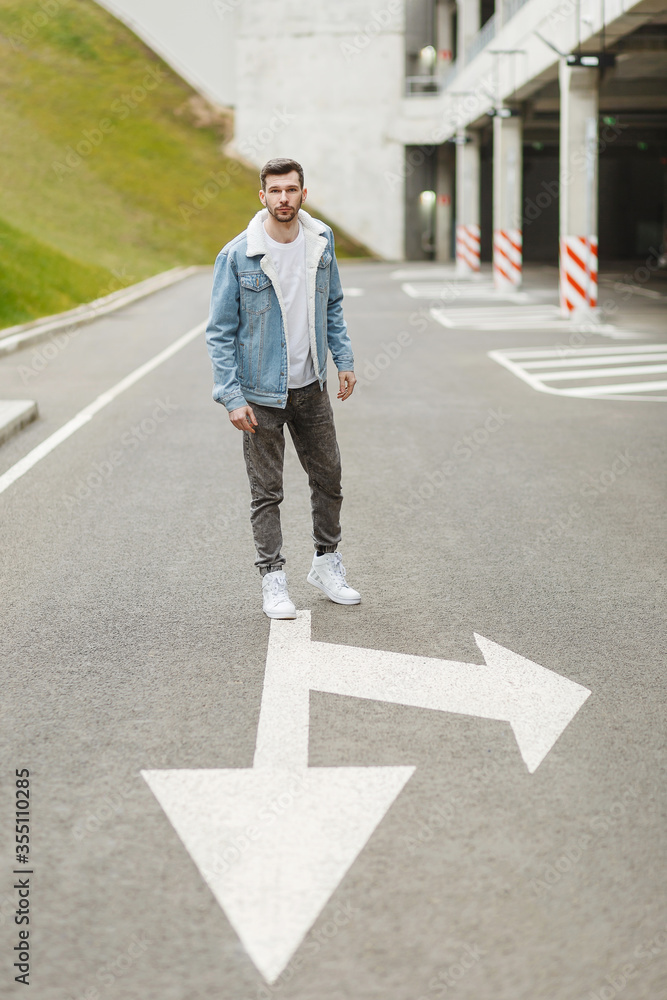 guy in a denim jacket stands on an empty street