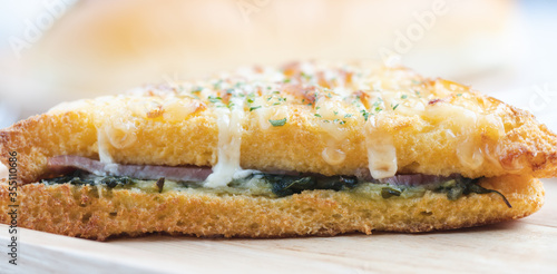 croque monsieur with slices of boiled ham, placed on a wooden plate with cooking tools.