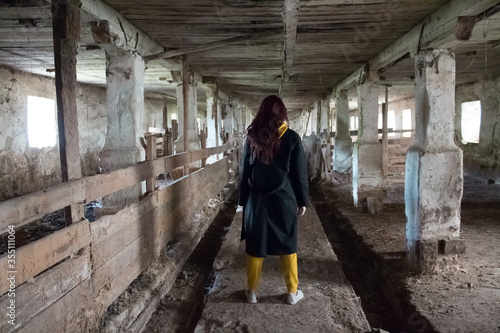  A girl in a gloomy abandoned building in a black cloak. Young woman in an industrial abandoned factory