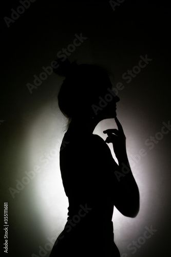 A shadow of a young woman shot into a white wall in profile. Silhouette of a woman on the wall.