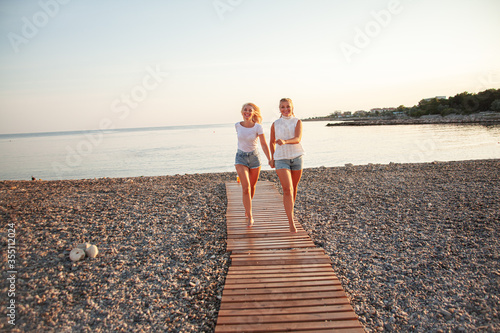 Two hot blond woman running on the uninhabited beach. the lifestyle of people are the happiness vacation. Girls dressed jeans shorts and t-shirt.
