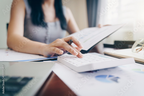 Woman entrepreneur using a calculator with a pen in her hand.Working from home with a calculator and financial report on wooden table. © nopparat