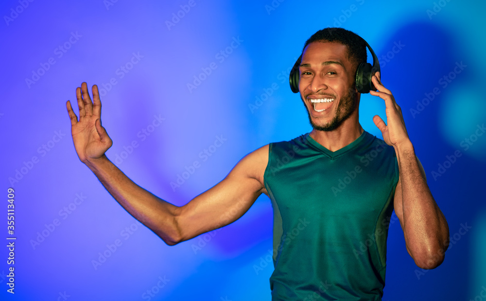 Excited African Guy Wearing Headphones Dancing During Training, Blue Background Excited African Guy Wearing Headphones Dancing During Training, Blue Background