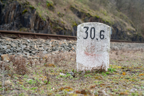 A white-painted milestone in front of a train track. Focus on the miletone, the track is blurred by distance.