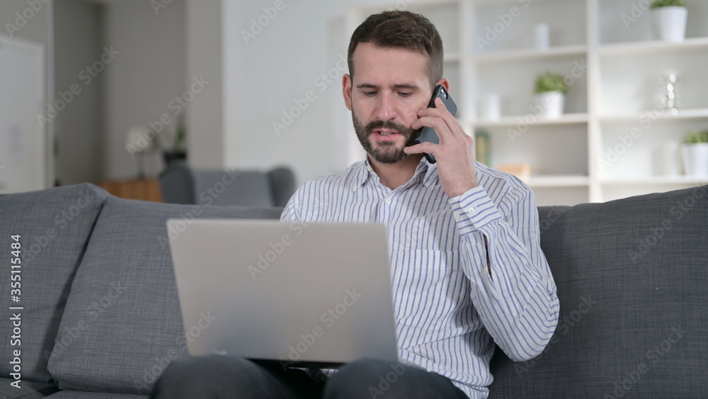 Young Man with Laptop Talking on Smartphone at Home Young Man with Laptop Talking on Smartphone at Home
