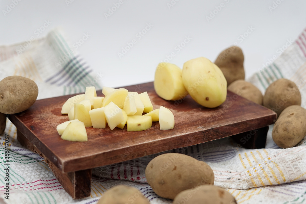 Pile of potato slice and unpeeled above wood cutting board Pile of potato slice and unpeeled above wood cutting board