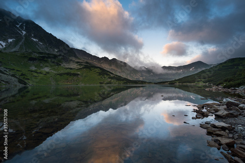 Hidden lake with reflection of mountains in it. Low clouds hanging above peaks.