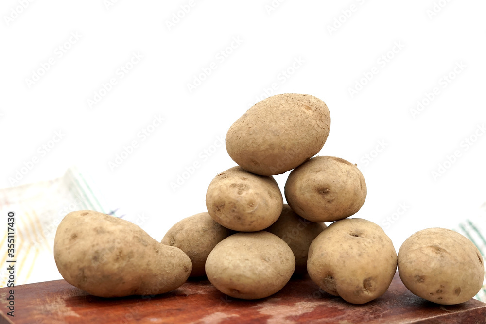 Pile of unpeeled potatoes above wood cutting board Pile of unpeeled potatoes above wood cutting board