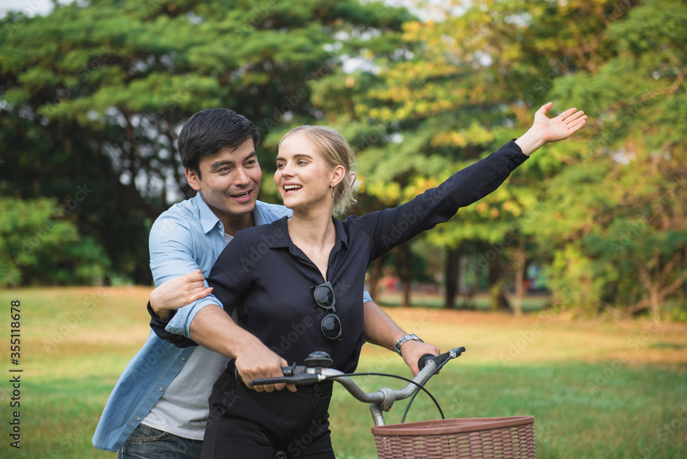Fototapeta premium Young couple walking their bike along happily talking in park