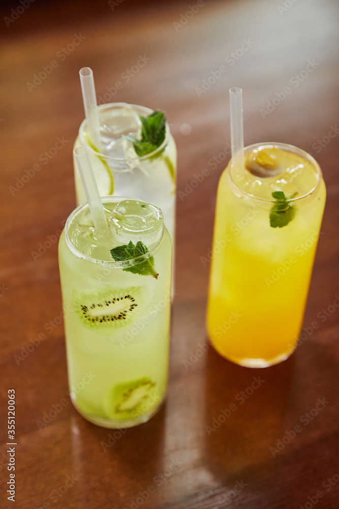 lemonade cocktails in glasses with straws and limes on wooden table, close view