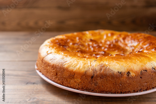 Freshly baked golden crust pie on a pink plate on a brown wooden table on the right. Space for text. Side view