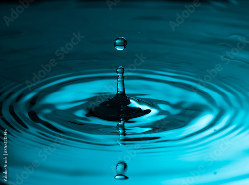 Water drop falling through the air. Small round ripples in a smooth surface and a reflection