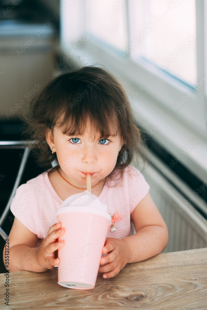 A little girl in a pink dress drinks from a pink cocktail glass sitting in the kitchen A little girl in a pink dress drinks from a pink cocktail glass sitting in the kitchen