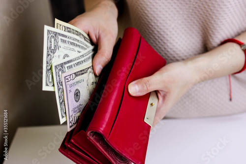Woman putting money into wallet on blurred background, closeup.