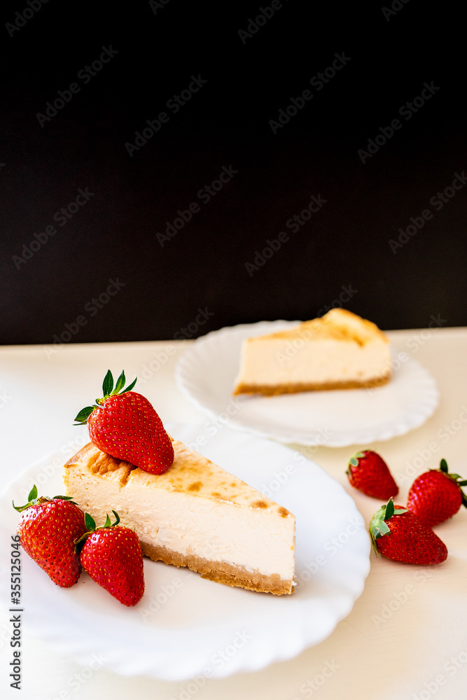 Close up of delicous cheesecake on white plates with organic home grown strawberries. Healthy food. Stay home. Cook home. Happy father's day gift. Holidays. Celebration. Dessert Close up of delicous cheesecake on white plates with organic home grown strawberries. Healthy food. Stay home. Cook home. Happy father's day gift. Holidays. Celebration. Dessert