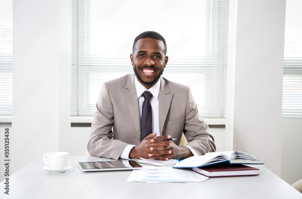 Happy handsome african american businessman smiling while looking at camera in office - obrazy, fototapety, plakaty 