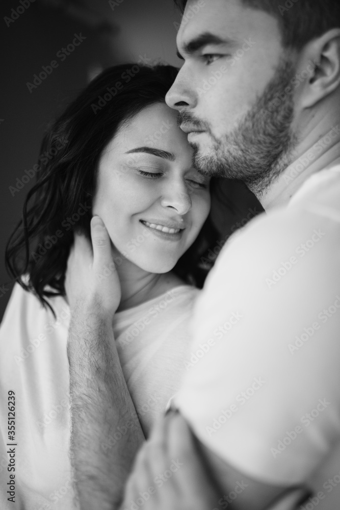 Close up cropped portrait of a couple in love together at home. Bearded brunette man gently touch with his hand face of her young dark long hair woman. Black and white photo. Close up cropped portrait of a couple in love together at home. Bearded brunette man gently touch with his hand face of her young dark long hair woman. Black and white photo.