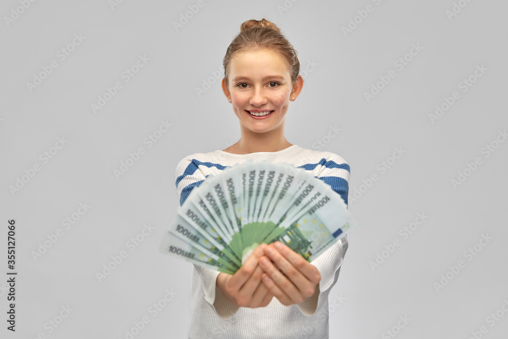 people concept - smiling teenage girl in pullover holding hundreds of euro money banknotes over grey background people concept - smiling teenage girl in pullover holding hundreds of euro money banknotes over grey background