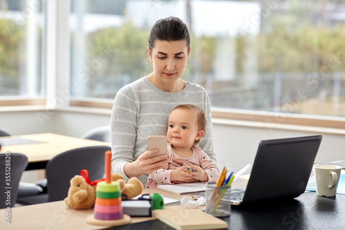 remote job, multi-tasking and family concept - mother with baby, smartphone and laptop working at home office