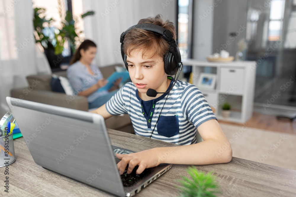 gaming, education and school concept - boy with laptop and headphones with microphone at home gaming, education and school concept - boy with laptop and headphones with microphone at home
