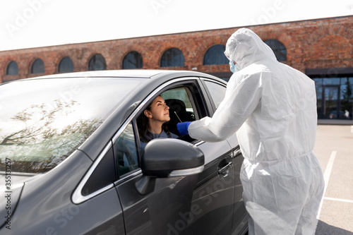 medicine, quarantine and pandemic concept - doctor or healthcare worker in protective gear or hazmat suit with cotton swab making coronavirus test for young woman in her car © Syda Productions