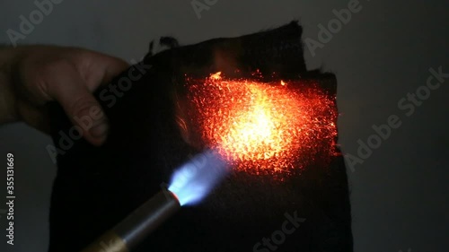 A man sets fire to a black fireproof fabric with a gas burner. Real time, contains people, fireproof material burns like coal red, but does not ignite.