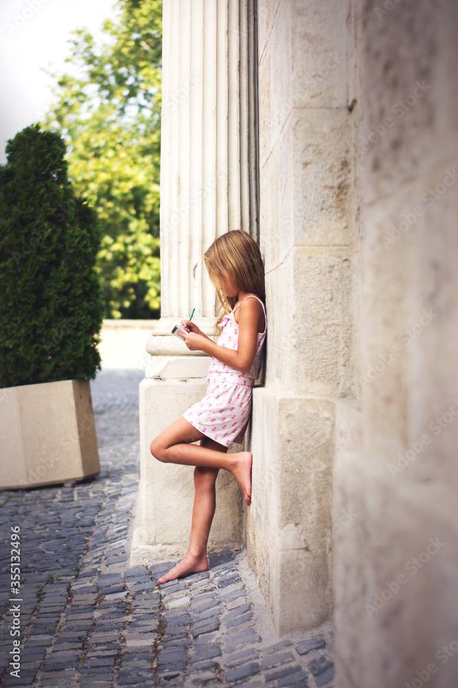 young girl standing and leaning on wall and writing, barefoot girl on the city Gyor