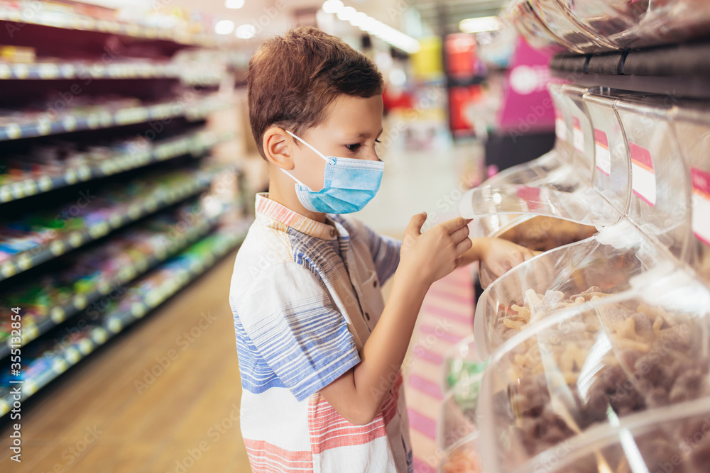 A new normal. Caucasian boy in sanitary face mask shopping sweets. Child wearing protective mask against coronavirus. Safety, health protection during covid-19 quarantine. A new normal. Caucasian boy in sanitary face mask shopping sweets. Child wearing protective mask against coronavirus. Safety, health protection during covid-19 quarantine.