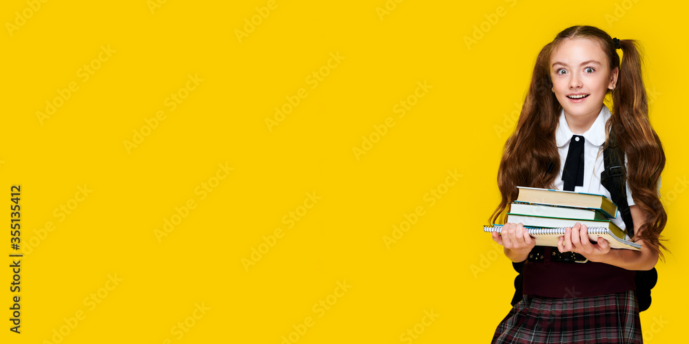 Caucasian elementary schoolgirl holds training books on yellow background, pupil wearing uniform Caucasian elementary schoolgirl holds training books on yellow background, pupil wearing uniform