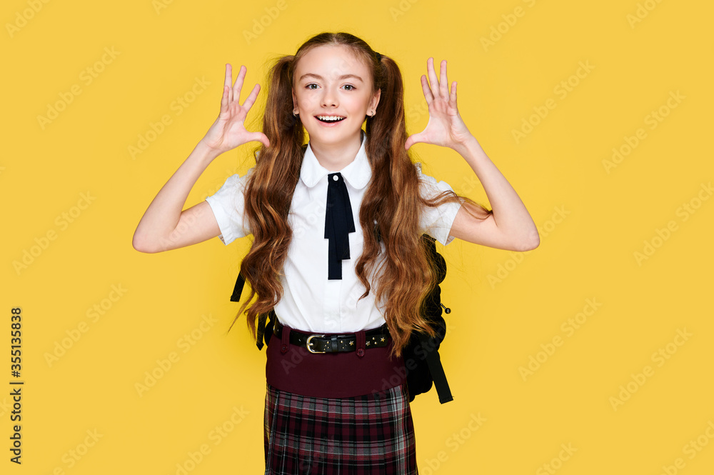 Young happy schoolgirl on bright vivid yellow background holding hands and heads, student in uniform and backpack Young happy schoolgirl on bright vivid yellow background holding hands and heads, student in uniform and backpack